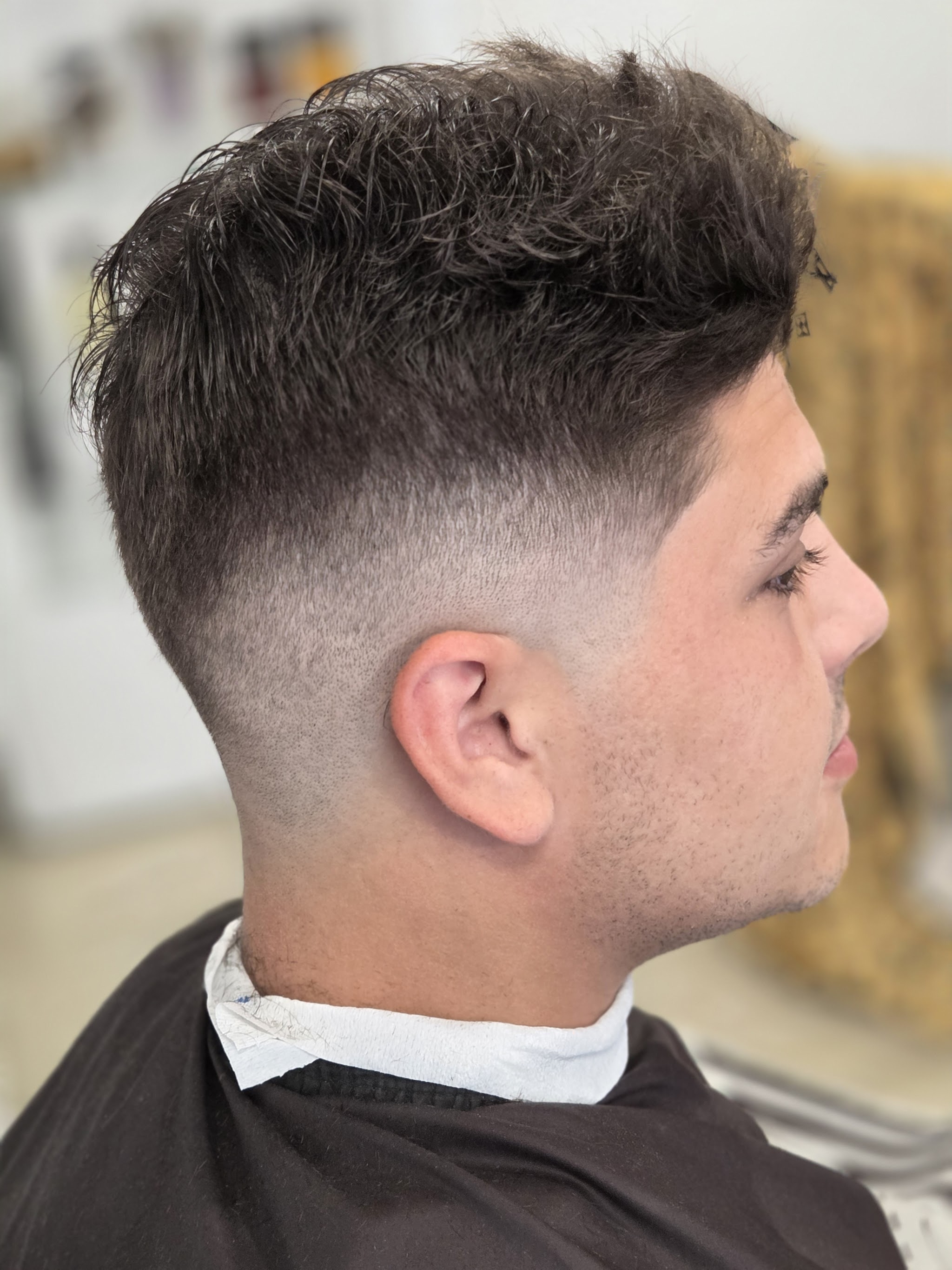Kapsel van opzij gezien, kort aan de zijkant en met textuur bovenop, geknipt bij Barbershop Monster