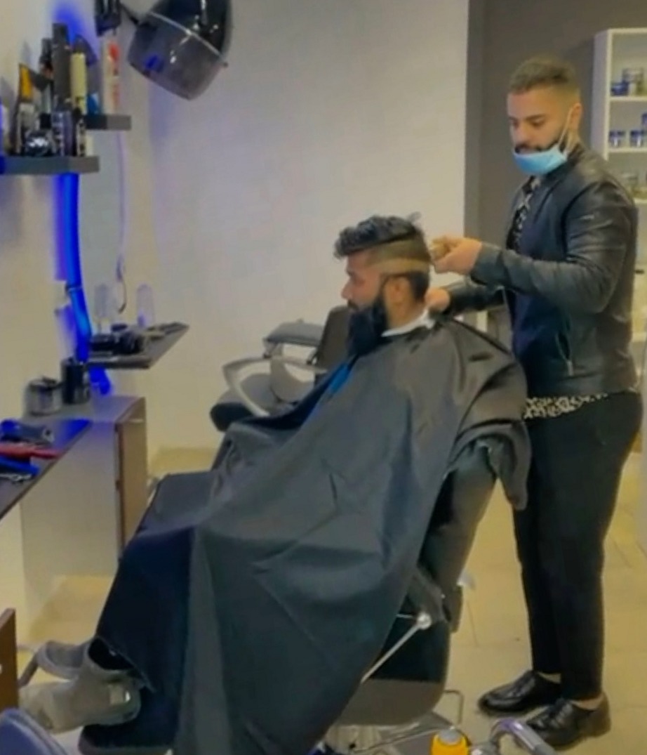 De barbier knipt een klant in de stoel, met blauw neonlicht langs de wand